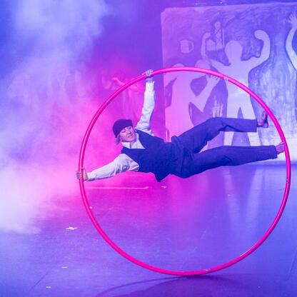 Performer w czerwonym hulajnodze na tle fioletowego i różowego oświetlenia, prezentujący akrobację w ramach Kulturatrium residency w Województwie Śląskim. (wygenerowano przez AI)