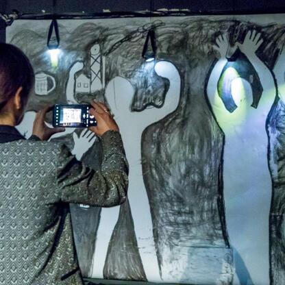 Osoba fotografuje monumentalny rysunek, iluminowany małymi światłami, związany z tematyką węgla i przemysłu. (wygenerowano przez AI)