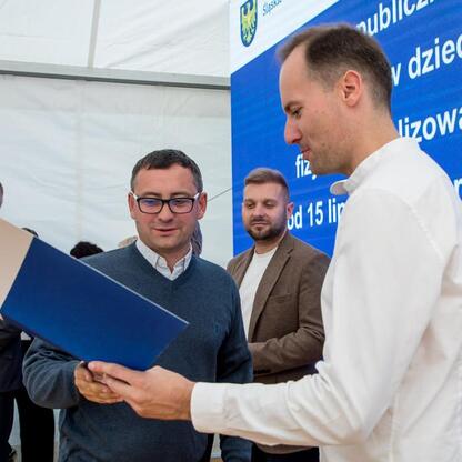 Wicemarszałek Leszek Pietraszek prezentuje symboliczny czek klubom sportowym na Superauto.pl Stadionie Śląskim. (wygenerowano przez AI)
