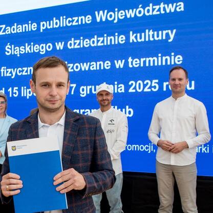 Grupa osób w Superauto.pl Stadionie Śląskim przed błękitnym plakatem o programie kulturalnym dla regionu. (wygenerowano przez AI)
