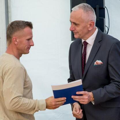 Leszek Pietraszek, wicemarszałek Województwa Śląskiego, prezentuje dokument przed Kajetanem Kajetanowiczem na Superauto.pl Stadionie Śląskim. (wygenerowano przez AI)