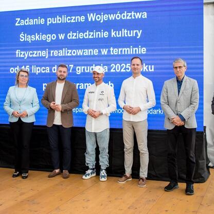 Grupa siedmiu osób na scenie w Superauto.pl Stadionie Śląskim podczas uroczystości wręczenia symbolicznych czeków. (wygenerowano przez AI)