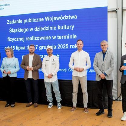 Grupa osiem osób na scenie Superauto.pl Stadionie Śląskim, uczestniczących w ceremonii Programu Klub, wspierającym kulturę fizyczną. (wygenerowano przez AI)