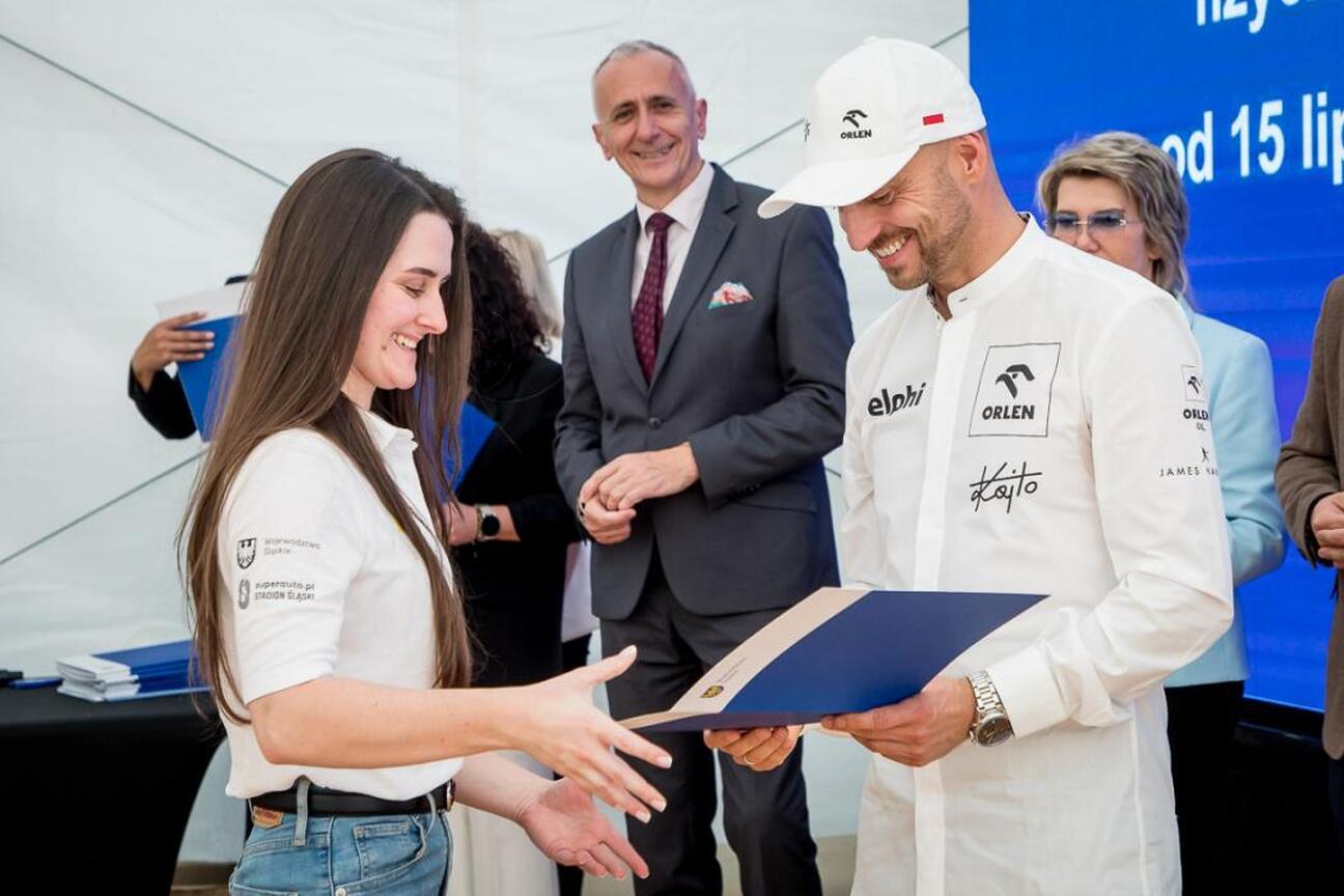 Dwa osoby w białych koszulkach z logo, uśmiechnięte, robią selfie na uroczystości Programu Klub, wspierającym sportowe kluby w regionie Śląskim. (wygenerowano przez AI)
