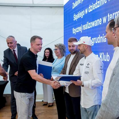 Wicemarszałek Leszek Pietraszek prezentuje symboliczne czeki przedstawicielom 154 klubów sportowych na Superauto.pl Stadionie Śląskim. (wygenerowano przez AI)
