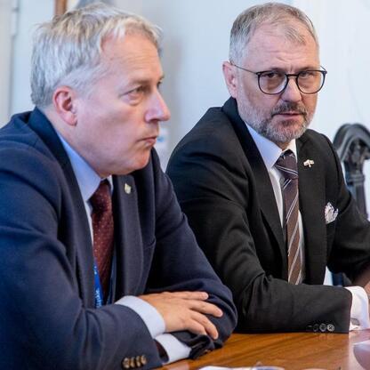 Dwóch mężczyzn w strojach formalnych siedzi przy stole, omawiając kwestie bezpieczeństwa energetycznego i przemysłu na Śląsku. (wygenerowano przez AI)