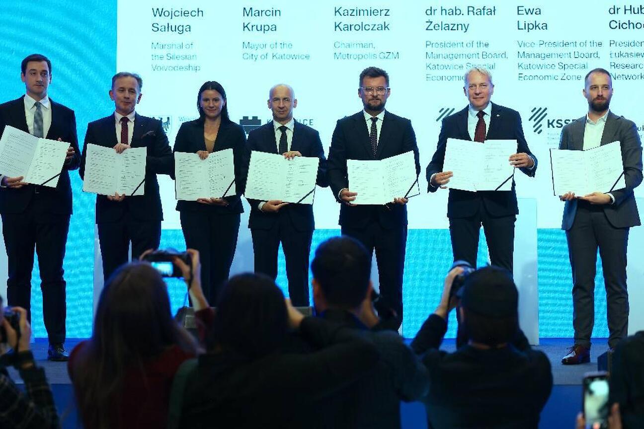 Grupa siedmiu kluczowych postaci z Kongresu Nowej Mobilności w Katowicach, podpisanie listu intencyjnego o współpracy w tworzeniu Centrum Nowej Mobilności. (wygenerowano przez AI)