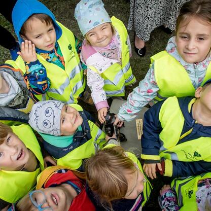 Grupa dzieci w żółtych kamizelkach ochronnych na tle parku, uczestniczące w edukacyjnej akcji geodezyjnej. (wygenerowano przez AI)