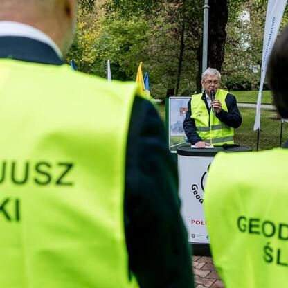 Mężczyzna w żółtym kamizelce ochrony przemysłowej przemawia na podium w Katowicach, podczas uroczystości odsłonięcia 