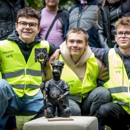 Grupa młodych ludzi w kamizelkach odblaskowych uczestniczy w uroczystości odsłonięcia nowego pomnika 