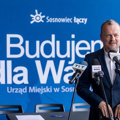 Mężczyzna przemawia na podium w Sosnowcu, podczas uroczystości związanych z transformacją byłego kopalni Kazimierz-Juliusz. (wygenerowano przez AI)