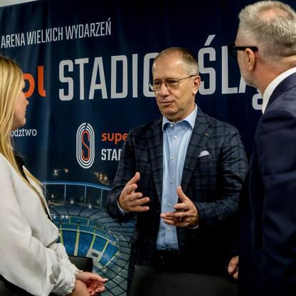 Na zdjęciu przedstawiono moment z konferencji prasowej 17. edycji Silesia Marathon, która odbywa się na Superauto.pl Stadion Śląski. Trzech osób dyskutuje o przygotowaniach do wydarzenia. (wygenerowano przez AI)