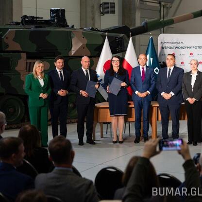 Grupa oficjalnych osób podczas ceremonii podpisania kontraktu na budowę nowoczesnych pojazdów opancerzonych w Bumar-Łabędy w Gliwicach. (wygenerowano przez AI)