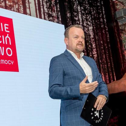 Na zdjęciu: Mężczyzna w niebieskim kraciastym garniturze prezentuje kampanię 