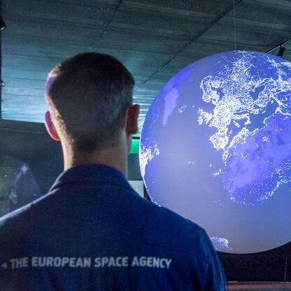 Mężczyzna w koszulce ESA obserwuje kulę ziemską w planetarium. (wygenerowano przez AI)