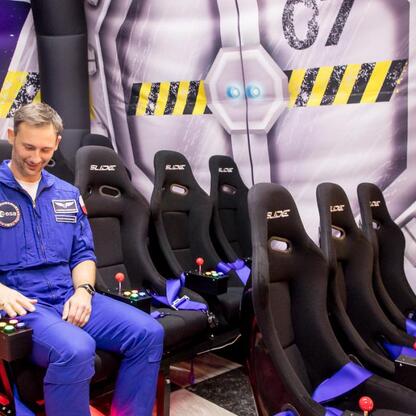 Astronauta dr Sławosz Uznański-Wiśniewski demonstruje symulator lotu w kosmosie w Planetarium Śląskim. (wygenerowano przez AI)