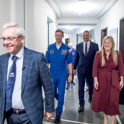 Grupa osób w kosmicznych kostiumach i formalnym stroju spaceruje po korytarzu w Śląskim Planetarium. (wygenerowano przez AI)