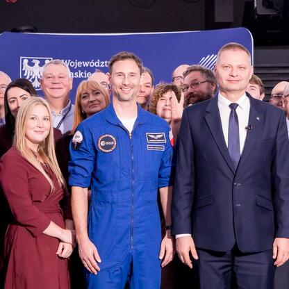 Astronauta w niebieskim strój kosmiczny, otoczony przez członków zarządu Województwa Śląskiego, podczas konferencji prasowej w Planetarium Śląskim. (wygenerowano przez AI)