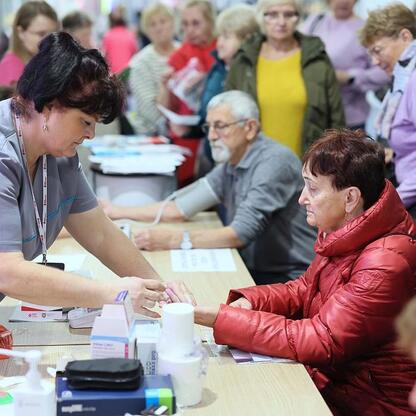 Zdjęcie przedstawia III edycję Centralnego Klubu Pacjenta na Stadionie Śląskim, gdzie lekarz pomaga osobie z badaniem ciśnienia. (wygenerowano przez AI)