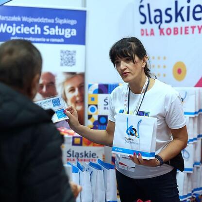 III edycja Centralnego Klubu Pacjenta na Stadionie Śląskim, gdzie wolontariuszka rozdaje materiały informacyjne. (wygenerowano przez AI)