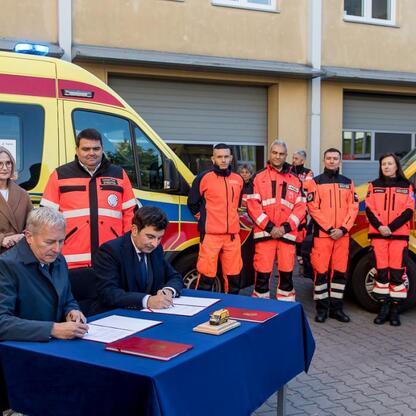 Wojciech Saługa, marszałek Województwa Śląskiego, podpisuje dokumenty wraz z wojewodą Markiem Wójcikiem i innymi uczestnikami uroczystości modernizacji floty ambulansów. (wygenerowano przez AI)