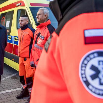 Grupa osób w mundurach Wojewódzkiego Pogotowia Ratunkowego przed nowoczesnym ambulansem. (wygenerowano przez AI)