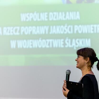 Kobieta z mikrofonem na konferencji o poprawie jakości powietrza w Śląsku. (wygenerowano przez AI)