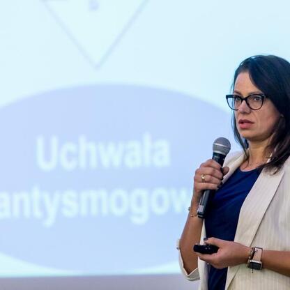 Na konferencji o poprawie jakości powietrza województwa śląskiego mówiąca z mikrofonem. (wygenerowano przez AI)