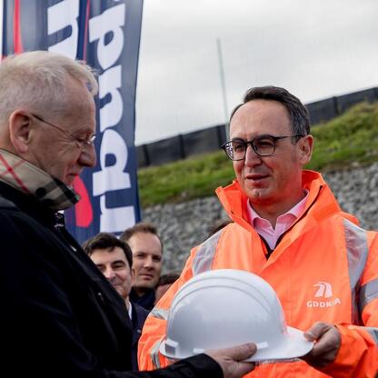 Grupa osób w strojach formalnych i ochronnych uczestniczy w ceremonii otwarcia odcinka S1, ważnej inwestycji w polskim regionie. (wygenerowano przez AI)
