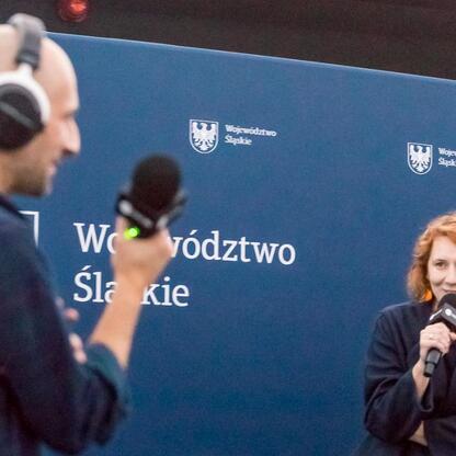 Ludzie z mikrofonami i słuchawkami na tle logo Śląskiego Voivodztwa. (wygenerowano przez AI)