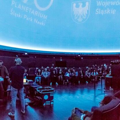 Wśród 280 słuchaczy w Planetarium Śląskiego podczas 208. notowania listy piosenek Radio 357, widoczna jest animacja kosmiczna na ekranie kopuły. (wygenerowano przez AI)
