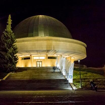 Planetarium Śląskiego nocą, oświetlone, z widocznymi drzewami i ciemnym niebem. (wygenerowano przez AI)