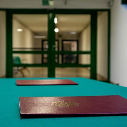 Marunowy dokument z emblematem leży na zielonym stole, tło: korytarz z drzwiami i schodami. (wygenerowano przez AI)