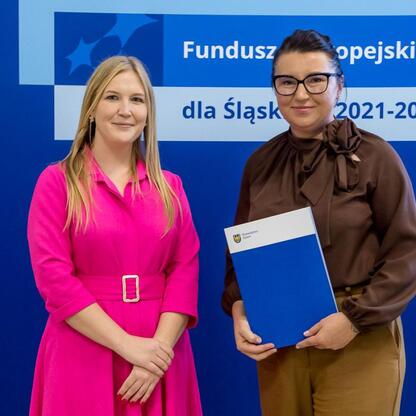 Joanna Bojczuk i inna osoba przedstawiają projekty z Europejskiego Funduszu dla Śląska 2021-2027. (wygenerowano przez AI)