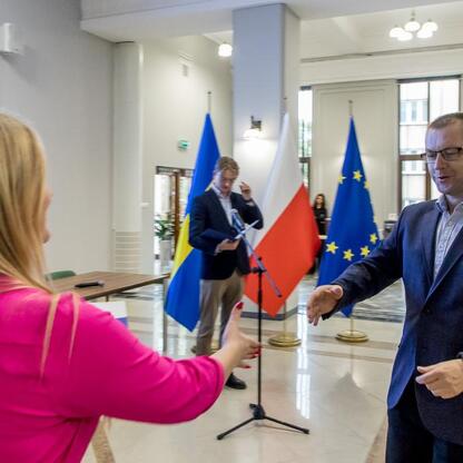 Formalna rozmowa w sali rządowej z flagami UE i polskimi, podkreślająca projekty europejskie. (wygenerowano przez AI)