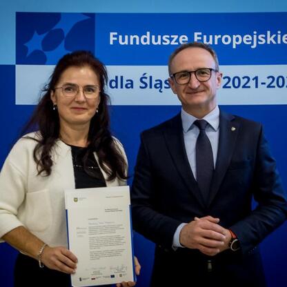 Grzegorz Boski i inny pracownik podczas ceremonii wręczenia listów gratulacyjnych w ramach programu Fundusze Europejskie dla Śląska 2021-2027. (wygenerowano przez AI)