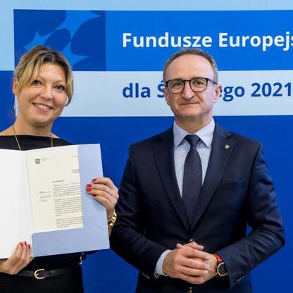 Wicemarszałek Grzegorz Boski i jego współpracownica prezentują dokumenty z projektów finansowanych ze środków europejskich dla Śląska 2021-2027. (wygenerowano przez AI)