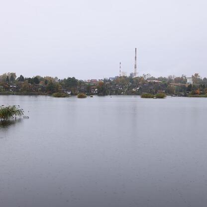 Jasne jezioro odbija chmurne niebo, w tle widoczna mała wioska z przemysłowym dymem. (wygenerowano przez AI)