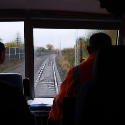Wnętrze kabiny maszynisty pociągu, z dwoma osobami w pomarańczowych kamizelkach ochronnych, siedzącymi i patrzącymi prosto, na tle ruchomego toru kolejowego. (wygenerowano przez AI)