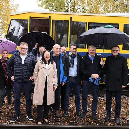 Grupa oficjalnych osób na torach kolejowych przed pociągiem, omawiając reaktywację linii Katowice-Jastrzębie. (wygenerowano przez AI)