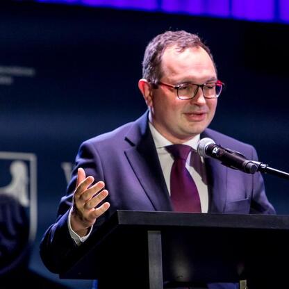 Podczas Forum Sołtysów w Koszęcinie, na podium stoi Marcin Ryś, który omawia konkurs „Piękna wieś Województwa Śląskiego”. (wygenerowano przez AI)