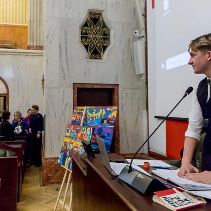 Formalna sesja Młodzieżowego Sejmiku Województwa Śląskiego, gdzie młody mężczyzna przemawia na podium, podkreślając znaczenie Tragedii Górnośląskiej. (wygenerowano przez AI)