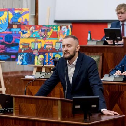 Formalna sesja Młodzieżowego Sejmiku Województwa Śląskiego, gdzie uczestnicy omawiają Tragedię Górnośląską, z mikrofonami i drewnianymi stołami. (wygenerowano przez AI)