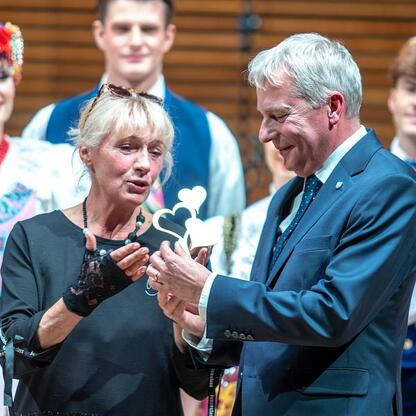 Marszałek Wojciech Saługa wręcza nagrodę na jubileuszowym koncercie dla seniorów w UTW Katowice. (wygenerowano przez AI)