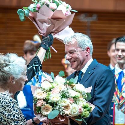Wojciech Saługa, Marszałek Województwa Śląskiego, odbiera bukiet kwiatów na jubileuszowym koncercie dla seniorów w Katowicach. (wygenerowano przez AI)
