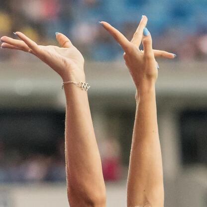 Zdjęcie przedstawia ręce z bransoletą z olimpijskimi pierścieniami, udekorowane niebieskimi paznokciami, podniesione w 