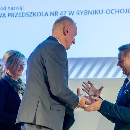 Podczas ceremonii wręczenia nagród za najlepszą przestrzeń publiczną województwa śląskiego, laureat otrzymuje od wicemarszałka Leszka Pietraszka nagrodę za rozbudowę przedszkola nr 47 w Rybniku-Ochojc (wygenerowano przez AI)