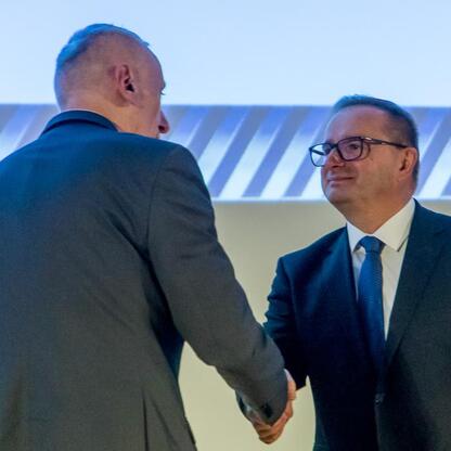 Dwóch mężczyzn w strojach formalnych trzyma się za ręce, nagradzani w konkursie Najlepsza Przestrzeń Publiczna Województwa Śląskiego. (wygenerowano przez AI)
