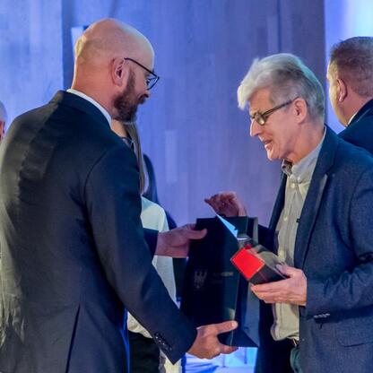 Podczas ceremonii wręczenia nagród za najlepszą przestrzeń publiczną województwa śląskiego, laureat odbiera nagrodę od wicemarszałka Leszka Pietraszka. (wygenerowano przez AI)
