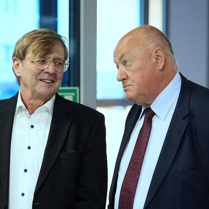 Dwóch mężczyzn w strojach formalnych omawiających zaawansowane technologie radioterapii adaptacyjnej w Katowickim Centrum Onkologii. (wygenerowano przez AI)